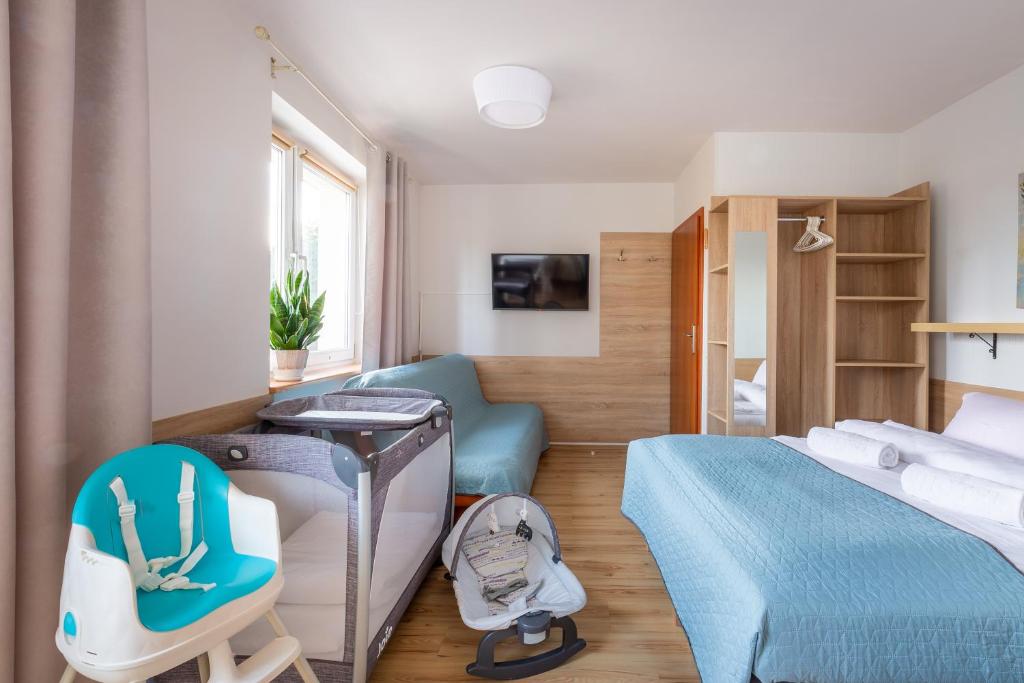Pokój z łóżkiem w niebieskiej pościeli, turkusowym krzesełkiem dziecięcym, turystycznym łóżeczkiem i bujakiem
