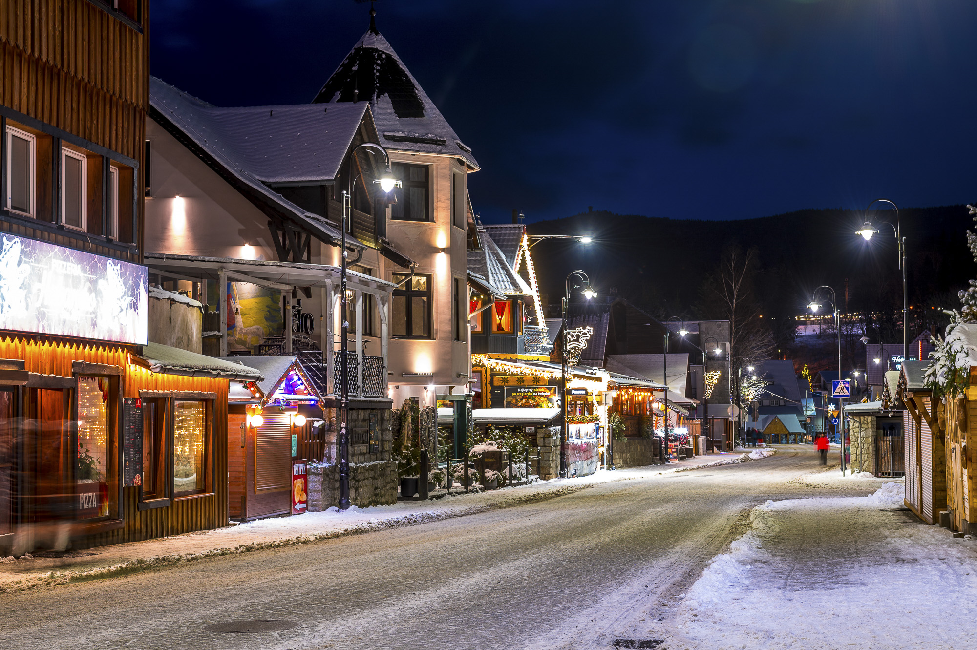 Zimowa nocna ulica z oświetlonymi drewnianymi domami, śniegiem i latarniami