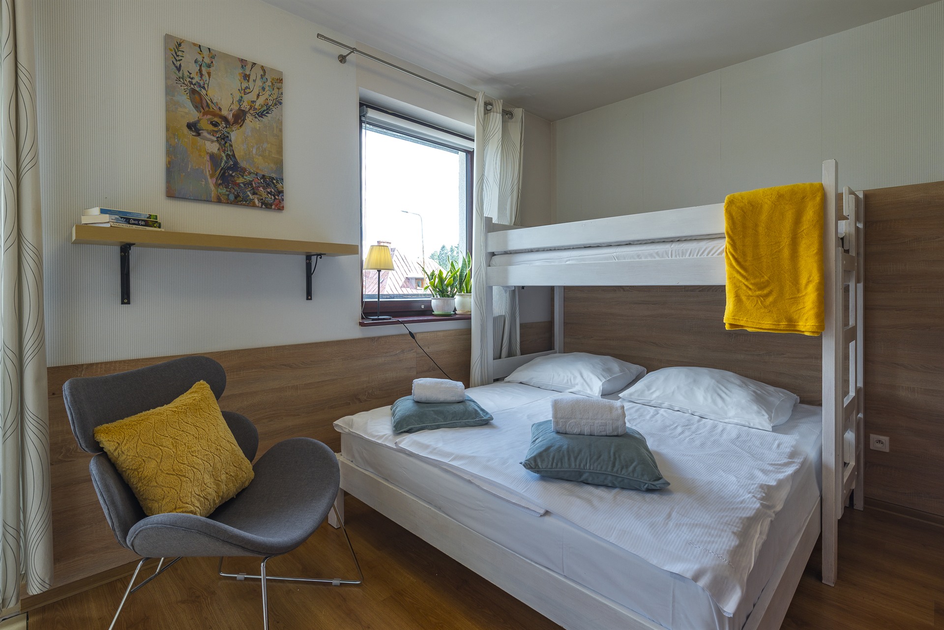 Pokój z białym łóżkiem piętrowym, dolnym podwójnym łóżkiem, żółty ręcznik, szary fotel z żółtą poduszką