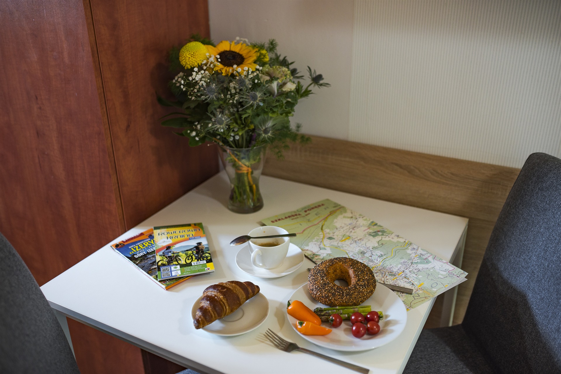 Stolik z bukietem słonecznika, filiżanką kawy, rogalikiem i talerzem z bajglem, pomidorkami i papryką