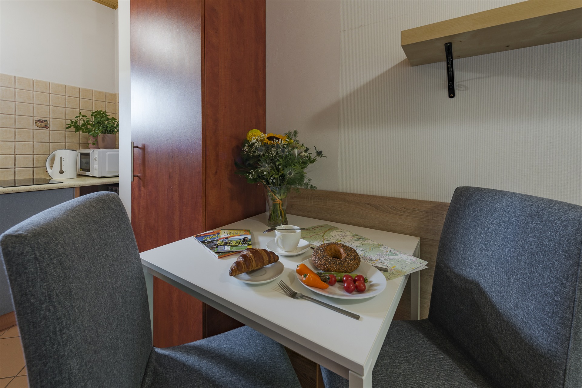 Stół z porannym śniadaniem: rogalik, sezamowy bajgiel, kawa, warzywa, bukiet kwiatów i rozłożona mapa