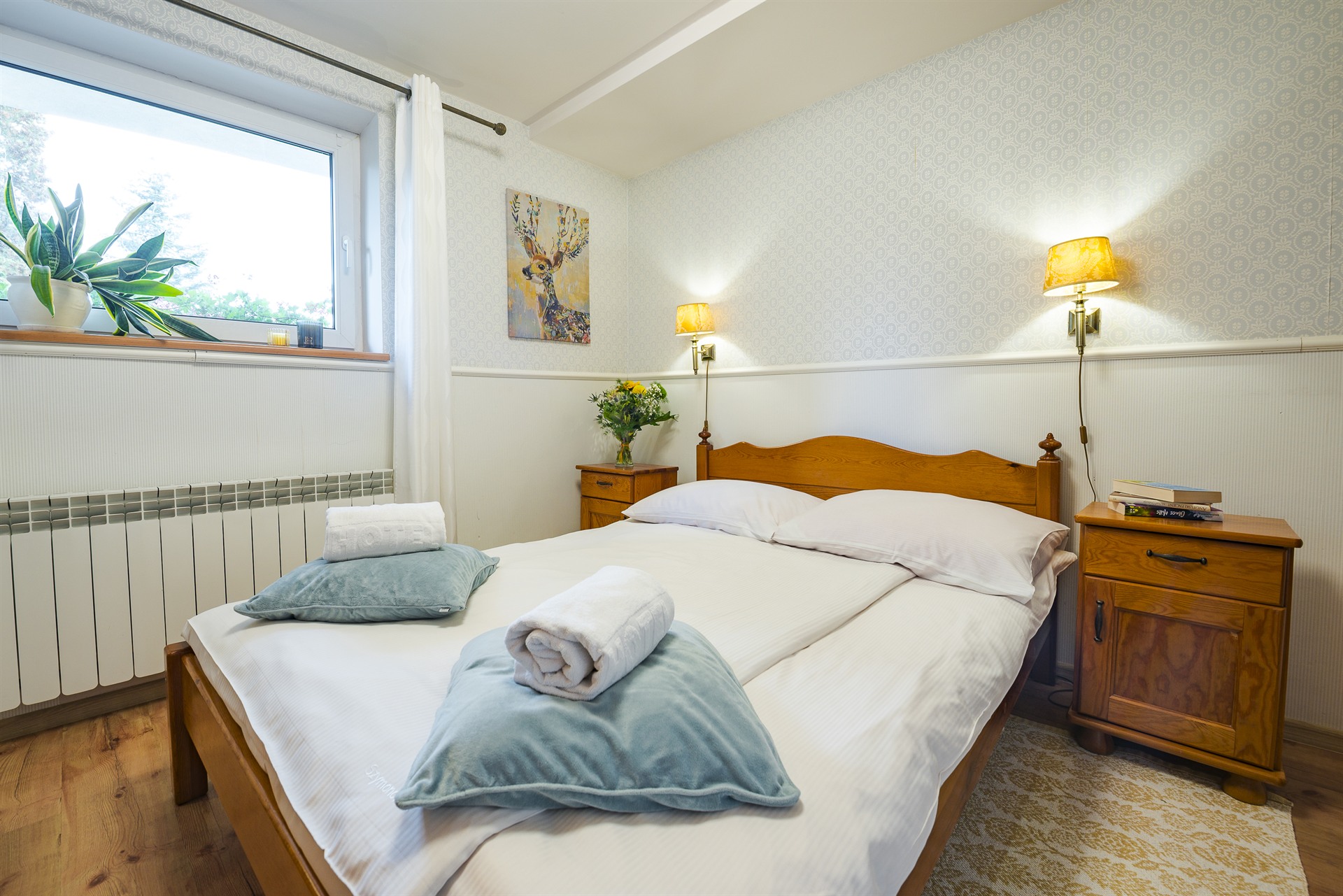 Drewniane łóżko z białą pościelą, miętowymi poduszkami i zwiniętymi ręcznikami, nocne stoliki z lampami