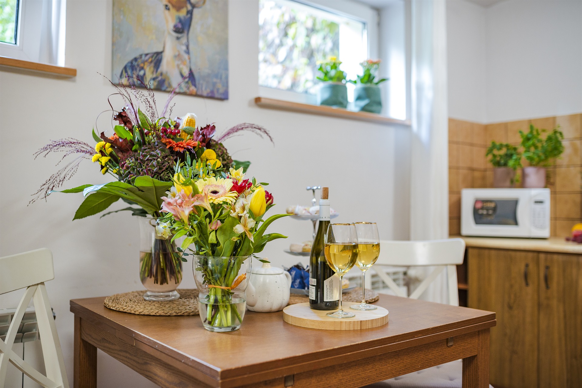 Stół z dwiema wazonami kolorowych kwiatów i butelką białego wina z dwoma kieliszkami w przytulnej kuchni