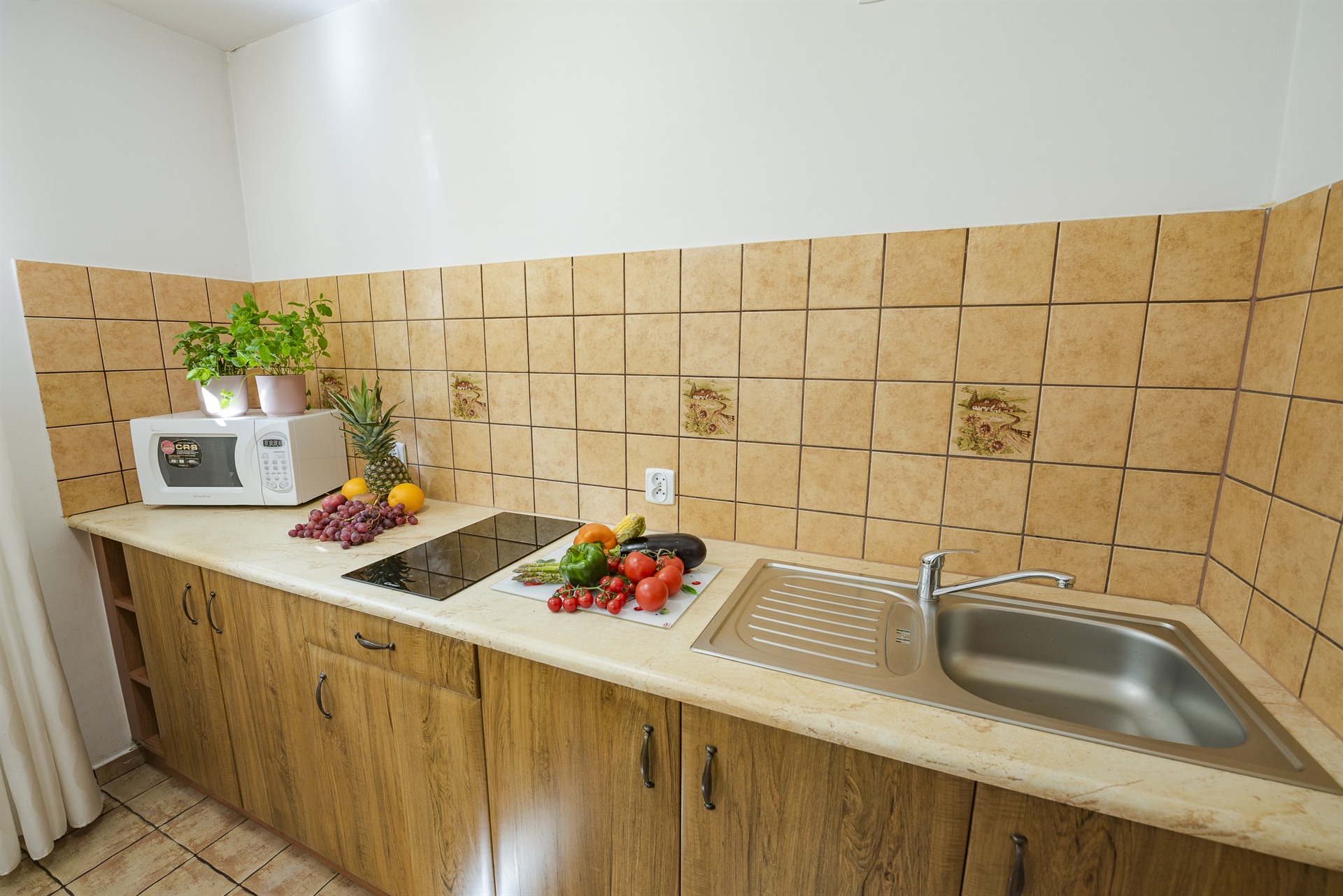 Kuchenny blat z umywalką, mikrofalówką, świeżymi warzywami i owocami oraz doniczkowymi roślinami