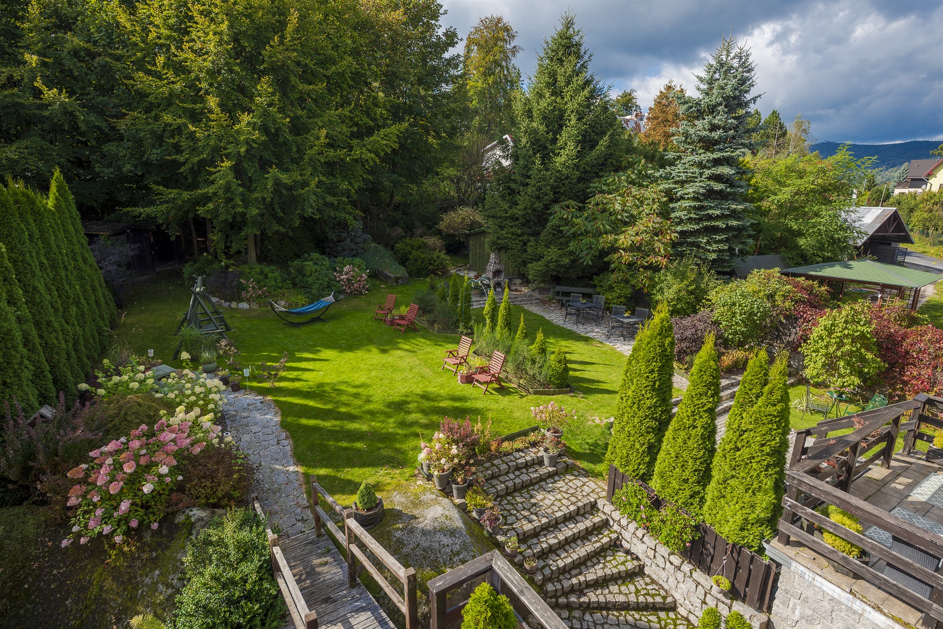 Zadbany ogród z zielonym trawnikiem, czerwonymi leżakami, hamakiem i kamiennymi schodami